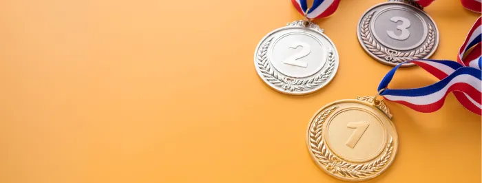 Trzy medale na pomarańczowym tle: złoty z numerem 1, srebrny z numerem 2 i brązowy z numerem 3